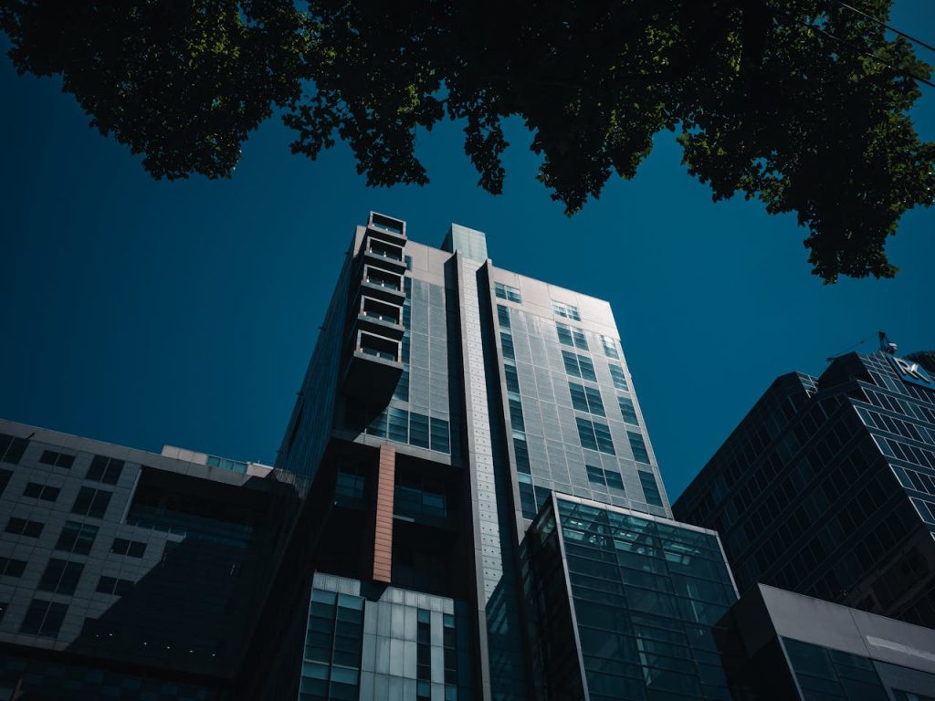 A modern skyscraper with glass facades rises against a clear blue sky, showcasing urban architecture.